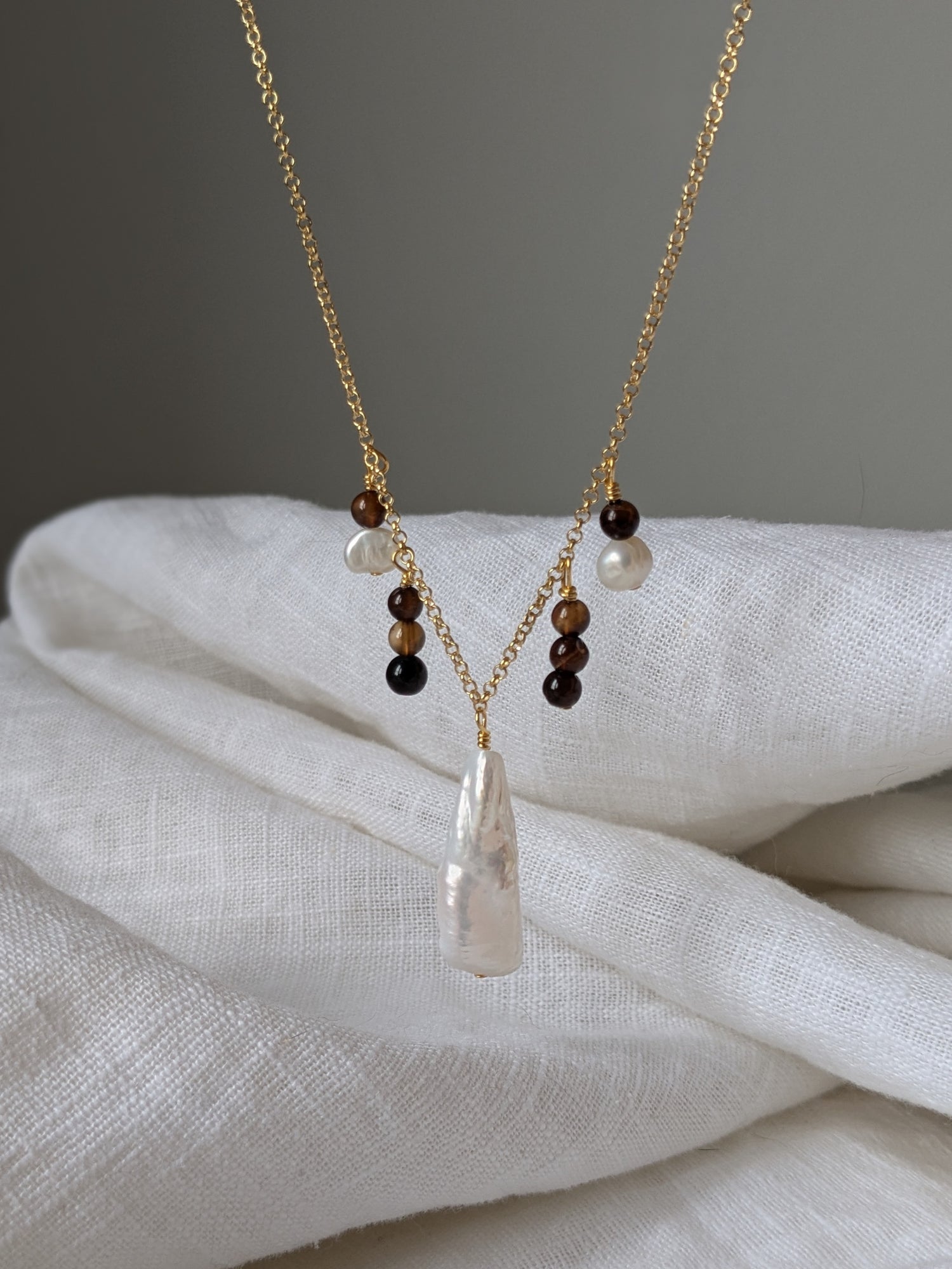A gold vermeil chain necklace with brown agate beads and ivory pearls, displayed on a white fabric.