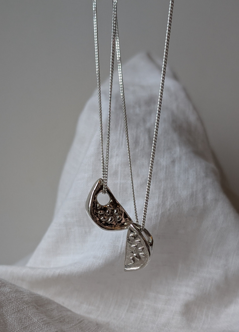 Two silver watermelon necklaces with pendants on a white fabric background
