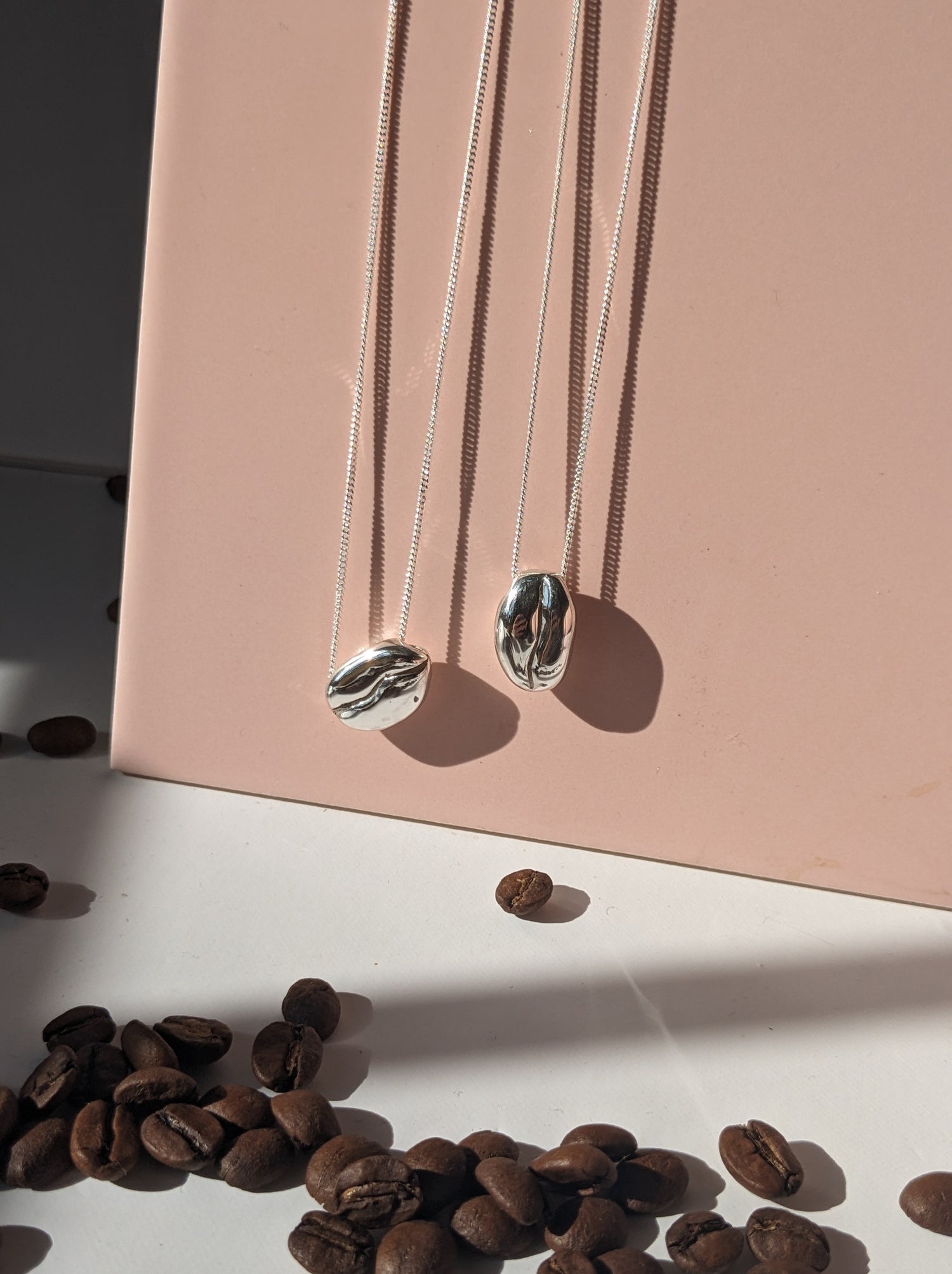 BArista Silver Coffee bean necklaces with real coffee beans on a pink tile background