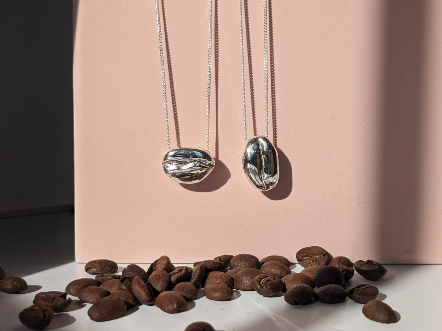 BArista Silver Coffee bean necklaces with real coffee beans on a pink tile background