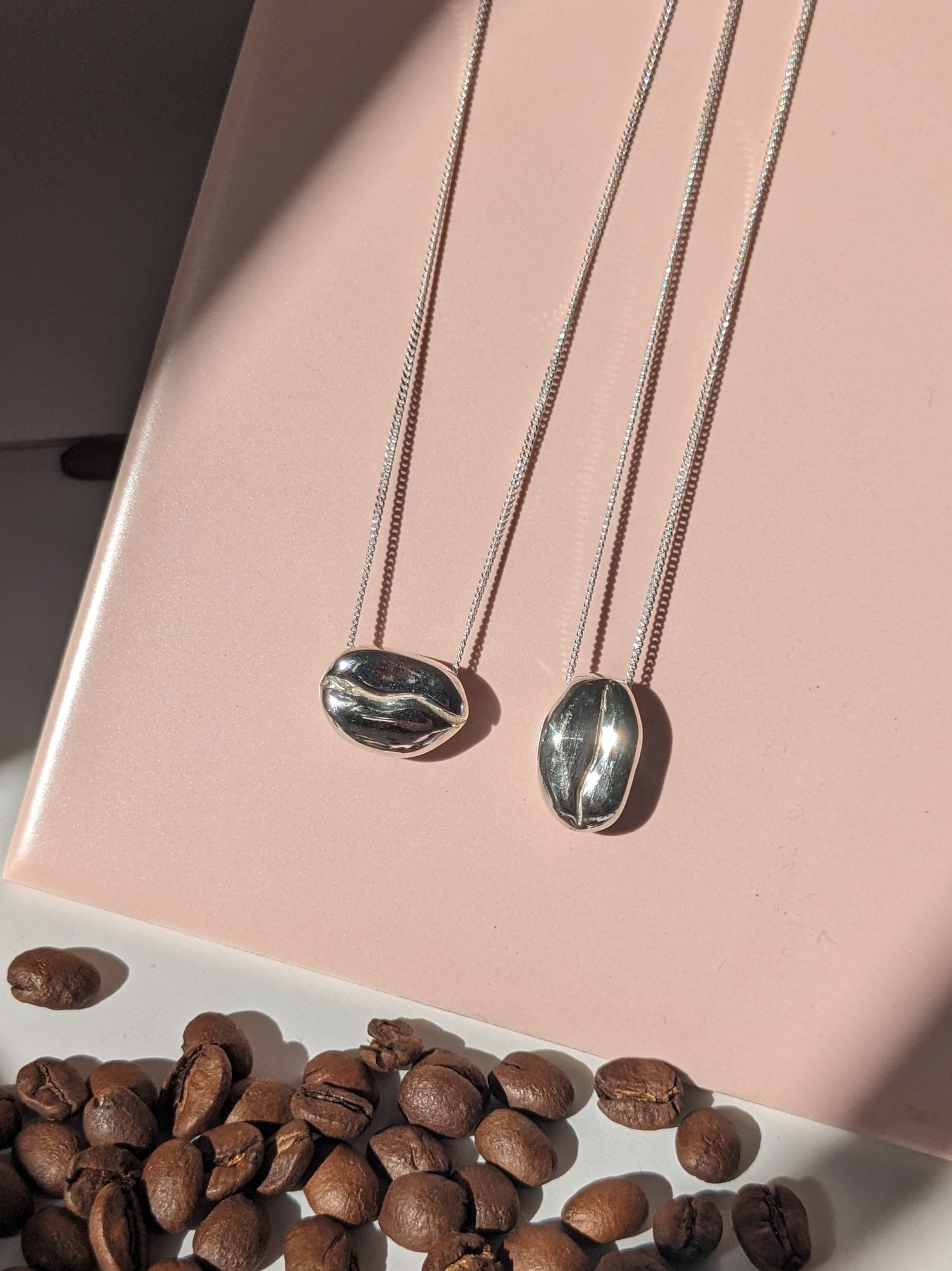 BArista Silver Coffee bean necklaces with real coffee beans on a pink tile background