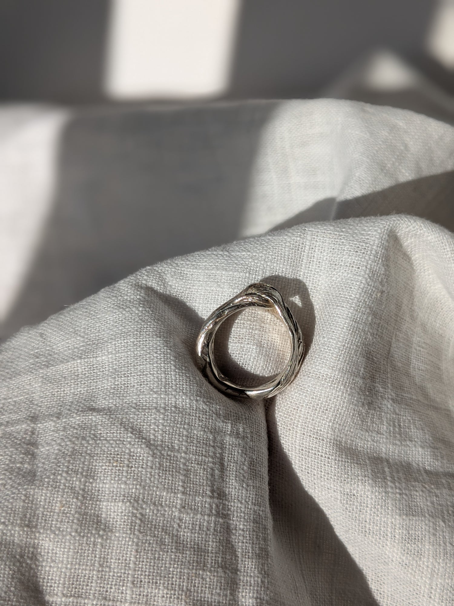 A silver ring with a twisted design and texture, displayed on a piece of fabric. Pretty Knot Mitsuor Hikime Silver Ring