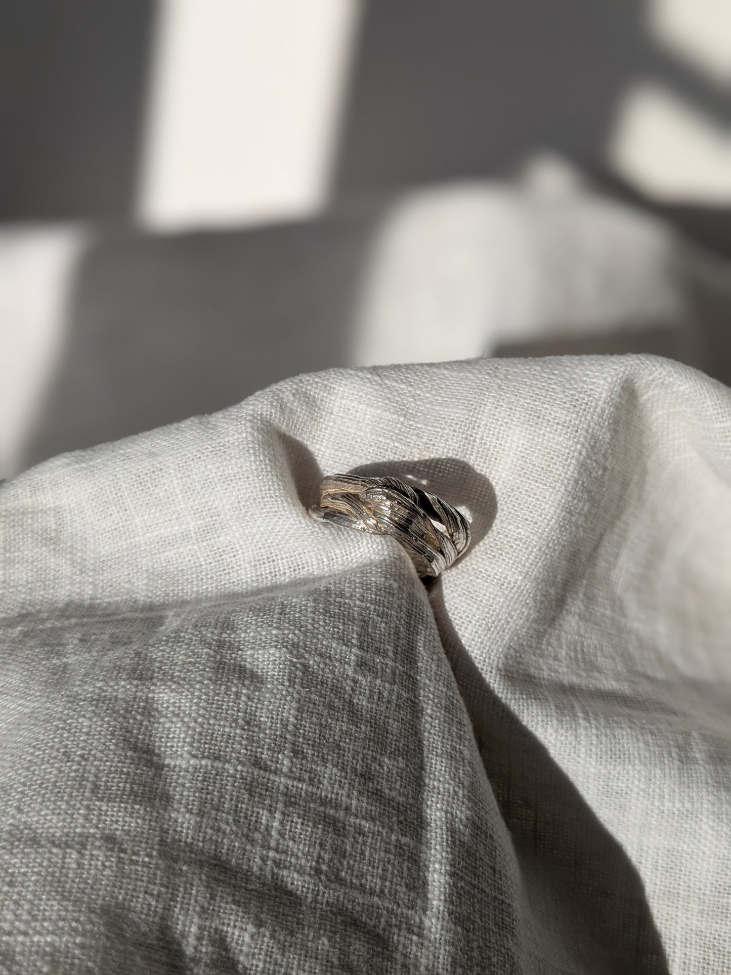 A silver ring with a twisted design and texture, displayed on a piece of fabric. Pretty Knot Mitsuro Hikime Silver Ring