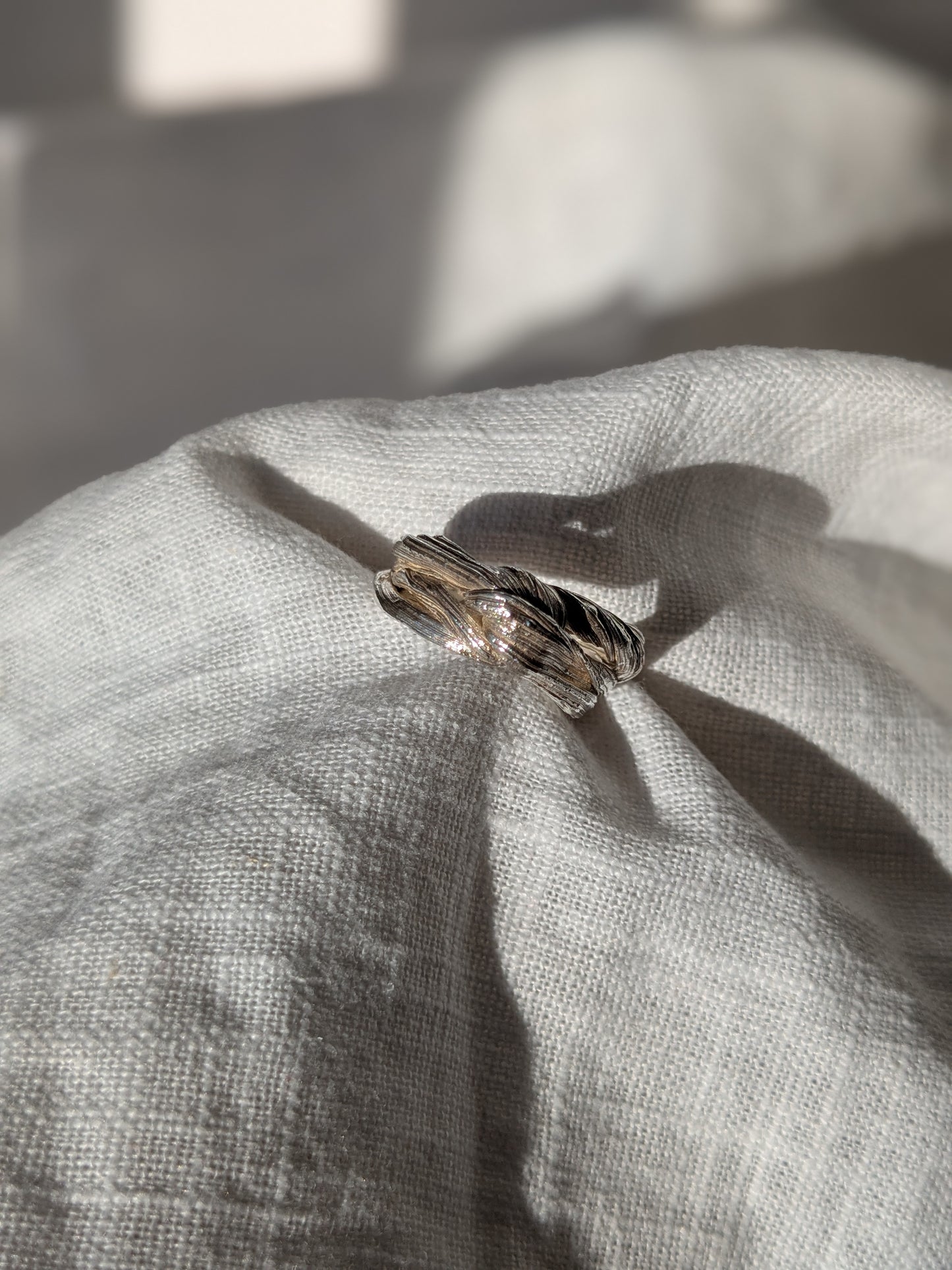 A silver ring with a twisted design and texture, displayed on a piece of fabric. Pretty Knot Mitsuor Hikime Silver Ring