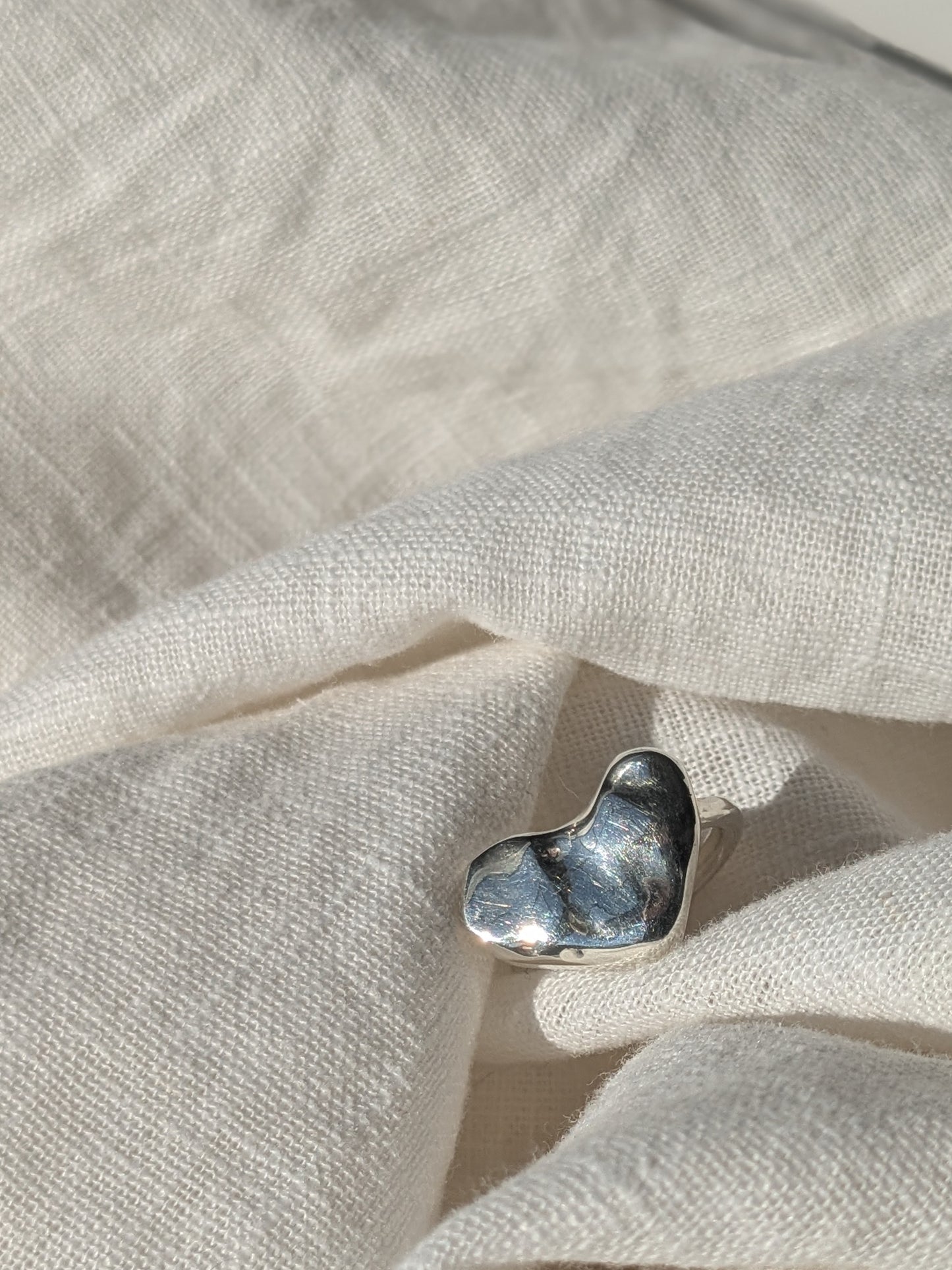 A silver heart-shaped ring placed on a grey fabric surface.