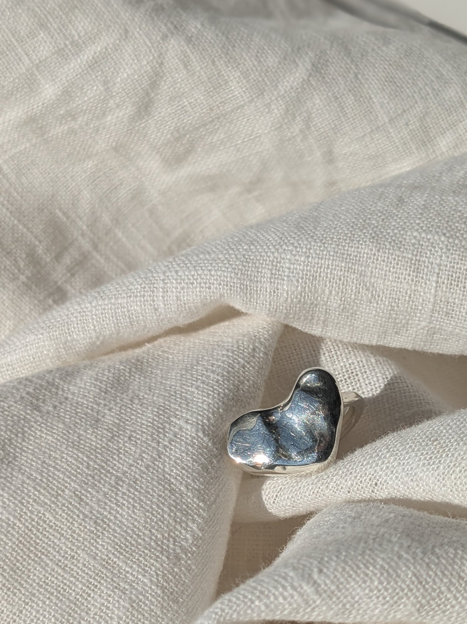 A silver heart-shaped ring placed on a grey fabric surface.