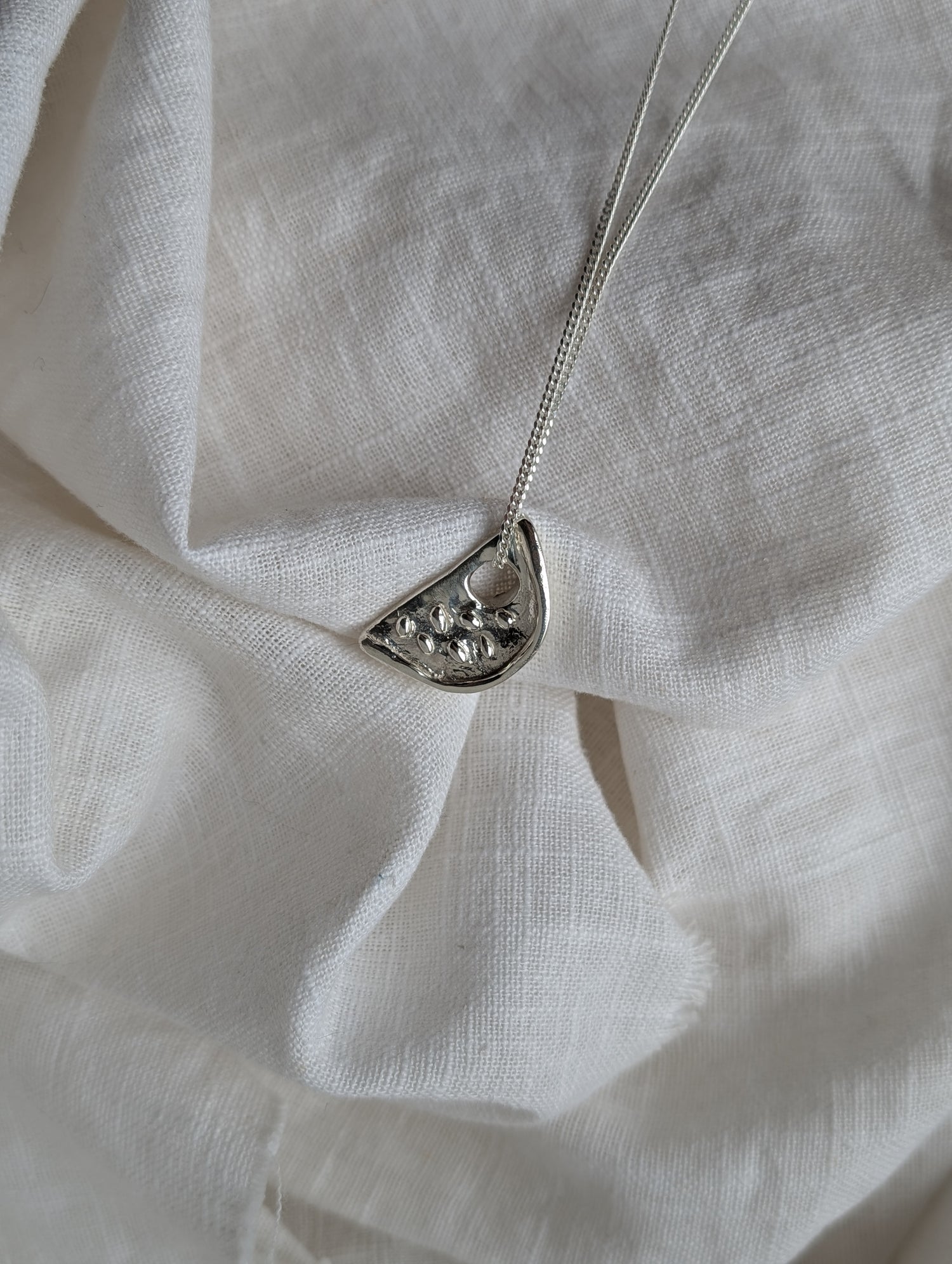 Silver watermelon necklace on a white linen background