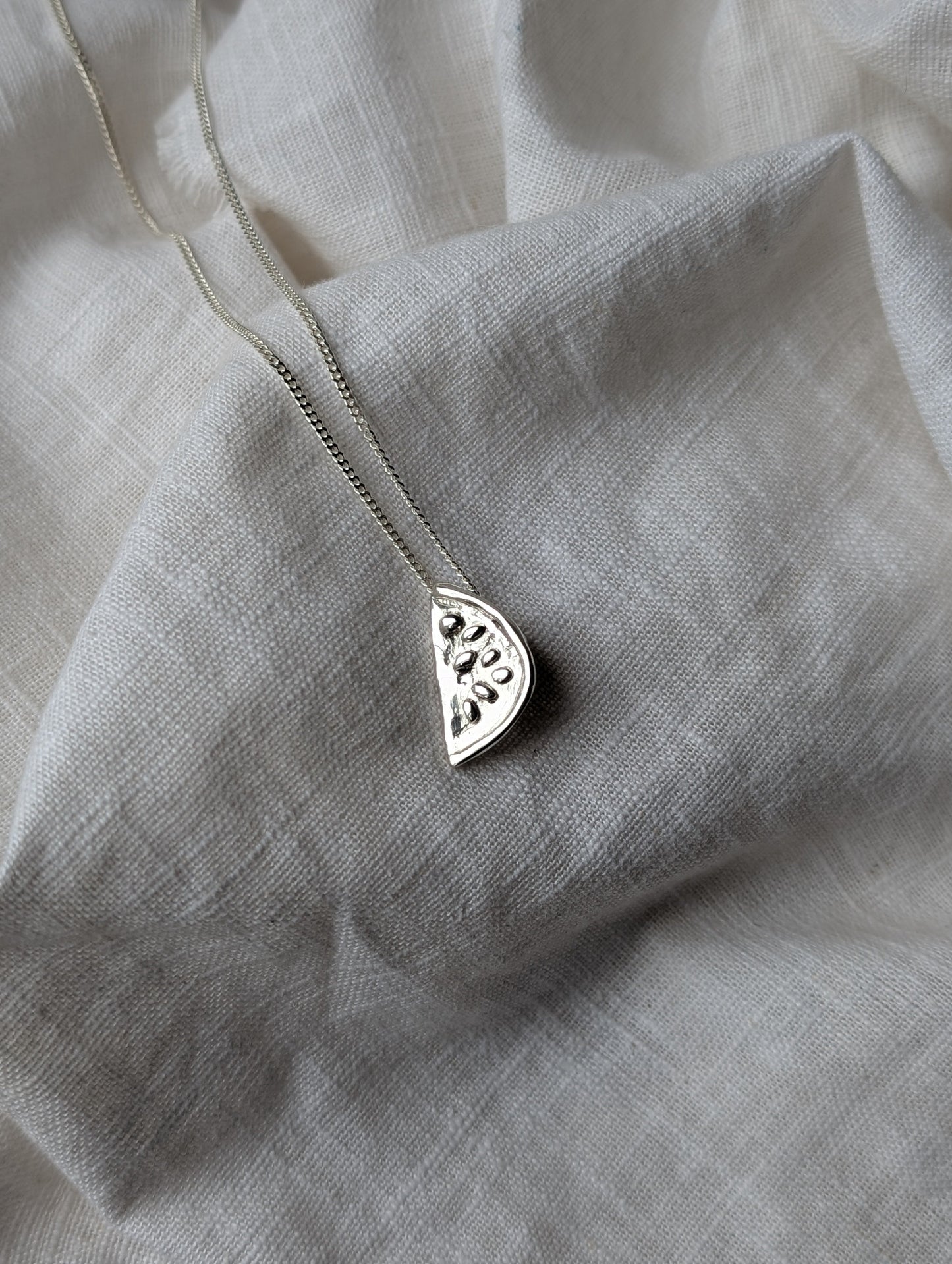 Silver watermelon necklace on a white linen background