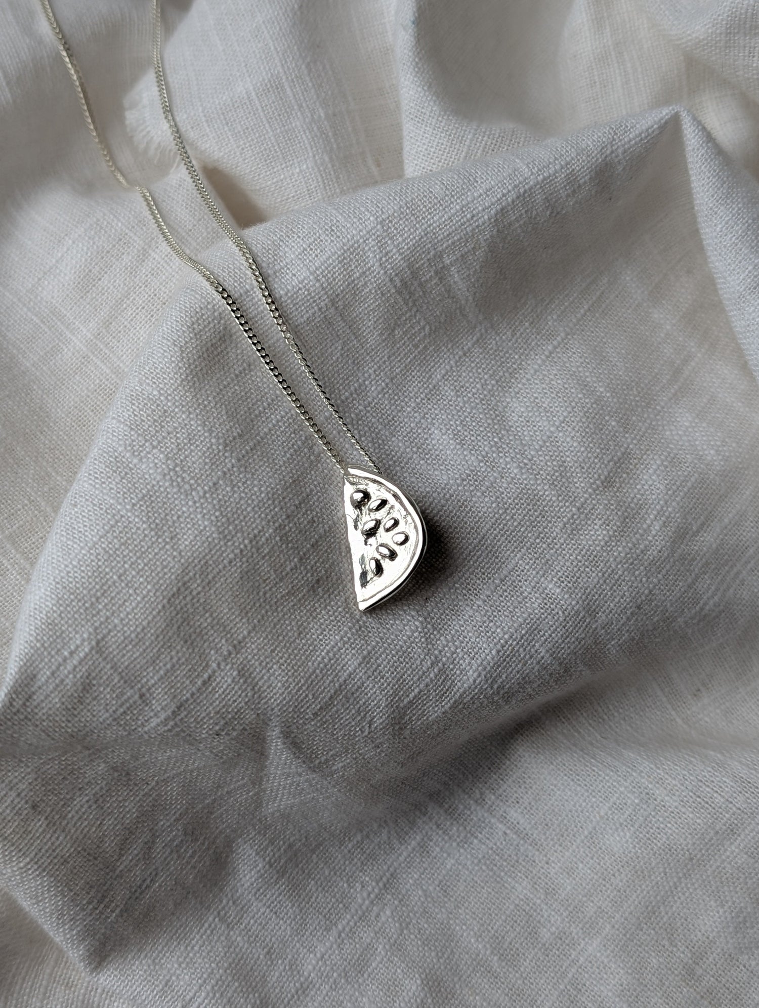 Silver watermelon necklace on a white linen background