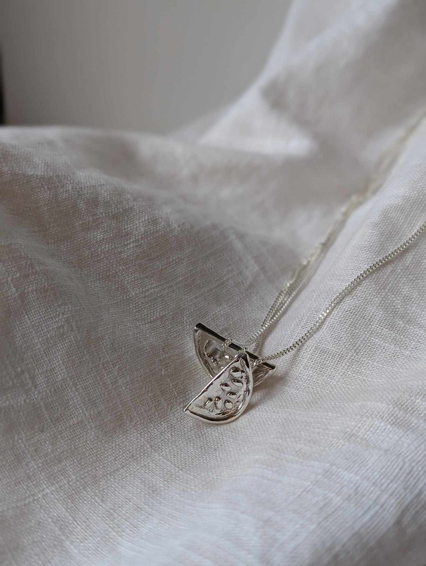 handmade silver watermelon necklaces on a white linen background