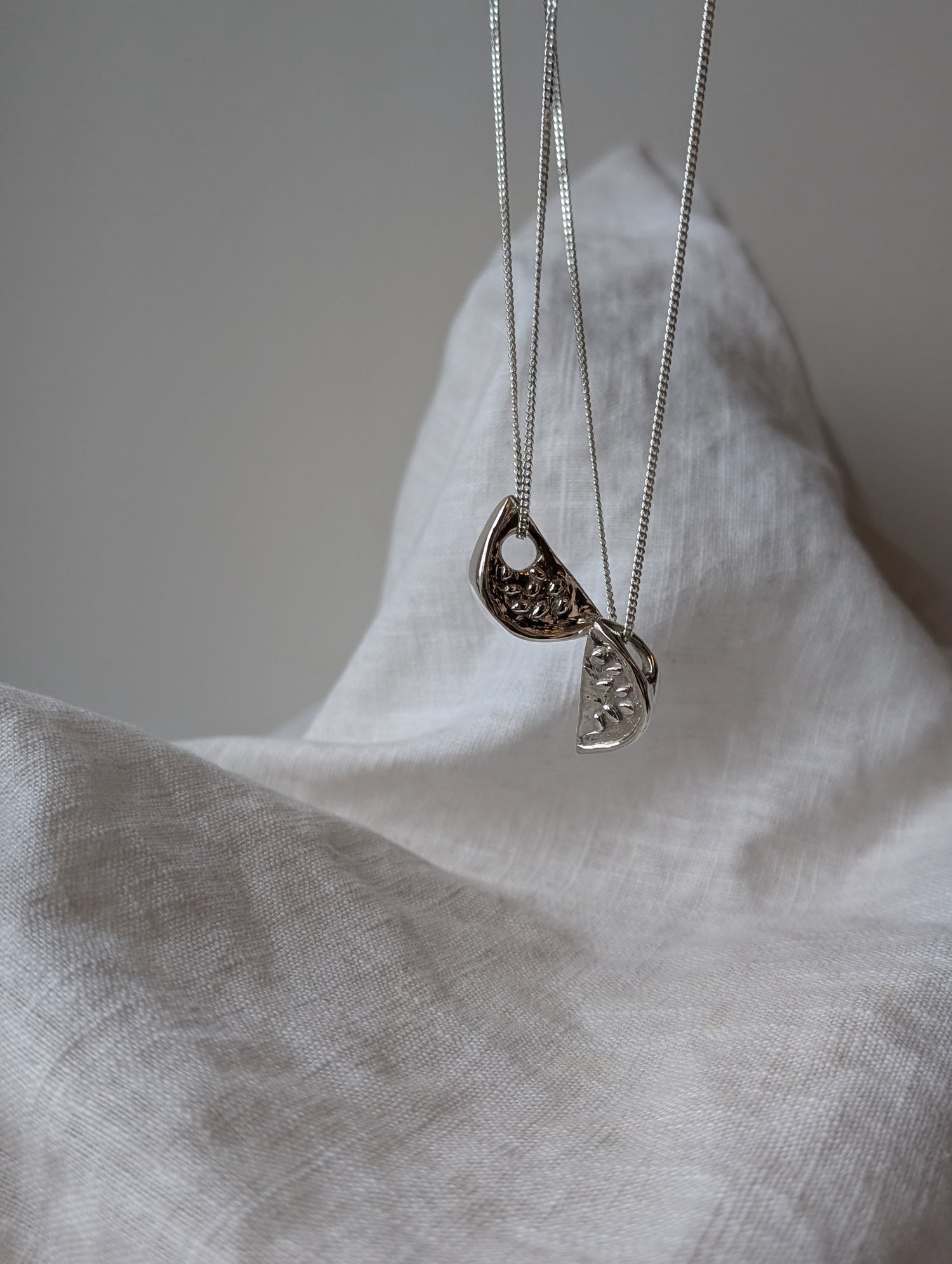 Two silver watermelon necklaces with pendants on a white fabric background