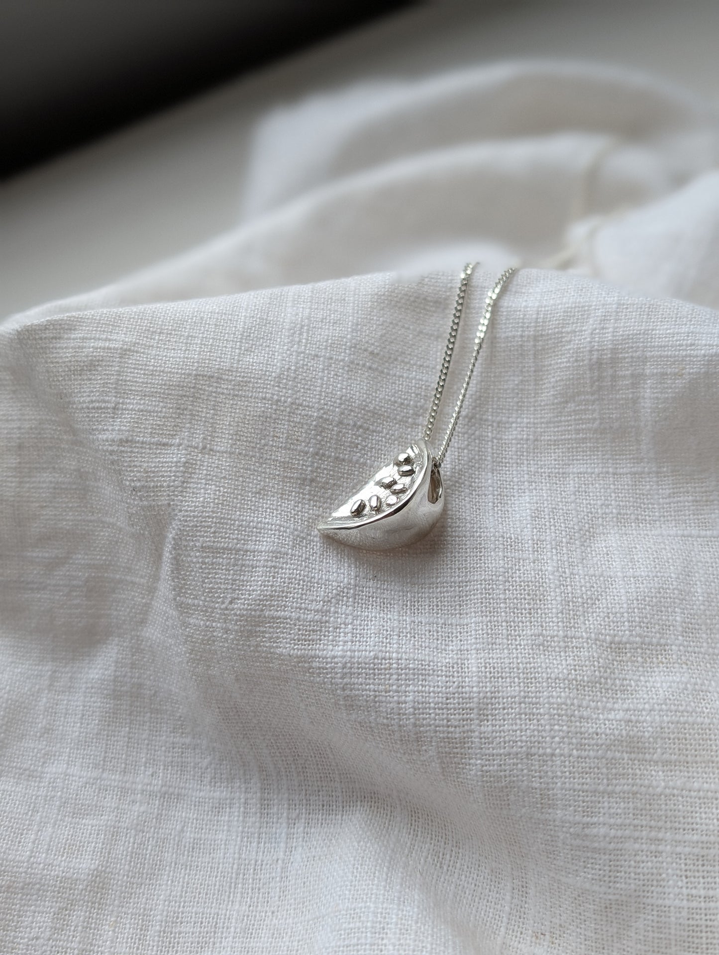 Silver watermelon necklace on a white linen background