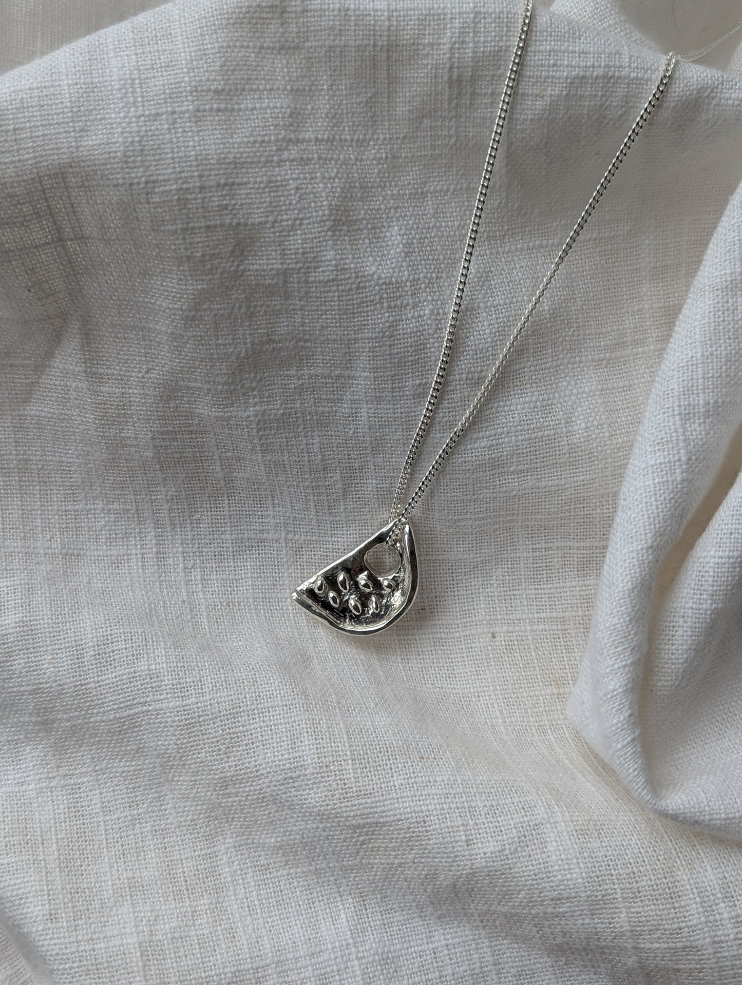 Silver watermelon necklace on a white linen background