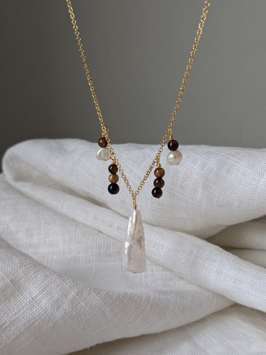 A gold vermeil chain necklace with brown agate beads and ivory pearls, displayed on a white fabric.