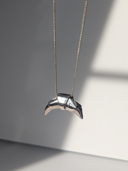 A silver croissant-shaped necklace pendant hanging on a chain, with a source of light creating a shadow and highlight on the pendant.